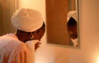 Woman with a towel wrapped around her hair drying her face in front of a mirror